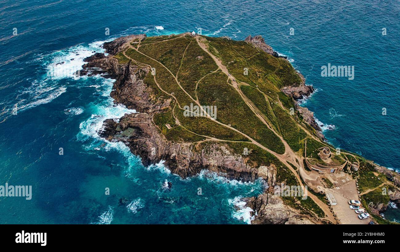 Vue aérienne d'une île côtière accidentée avec une végétation verte, des falaises rocheuses et des vagues s'écrasant contre le rivage. Un chemin sinueux mène à un phare Banque D'Images