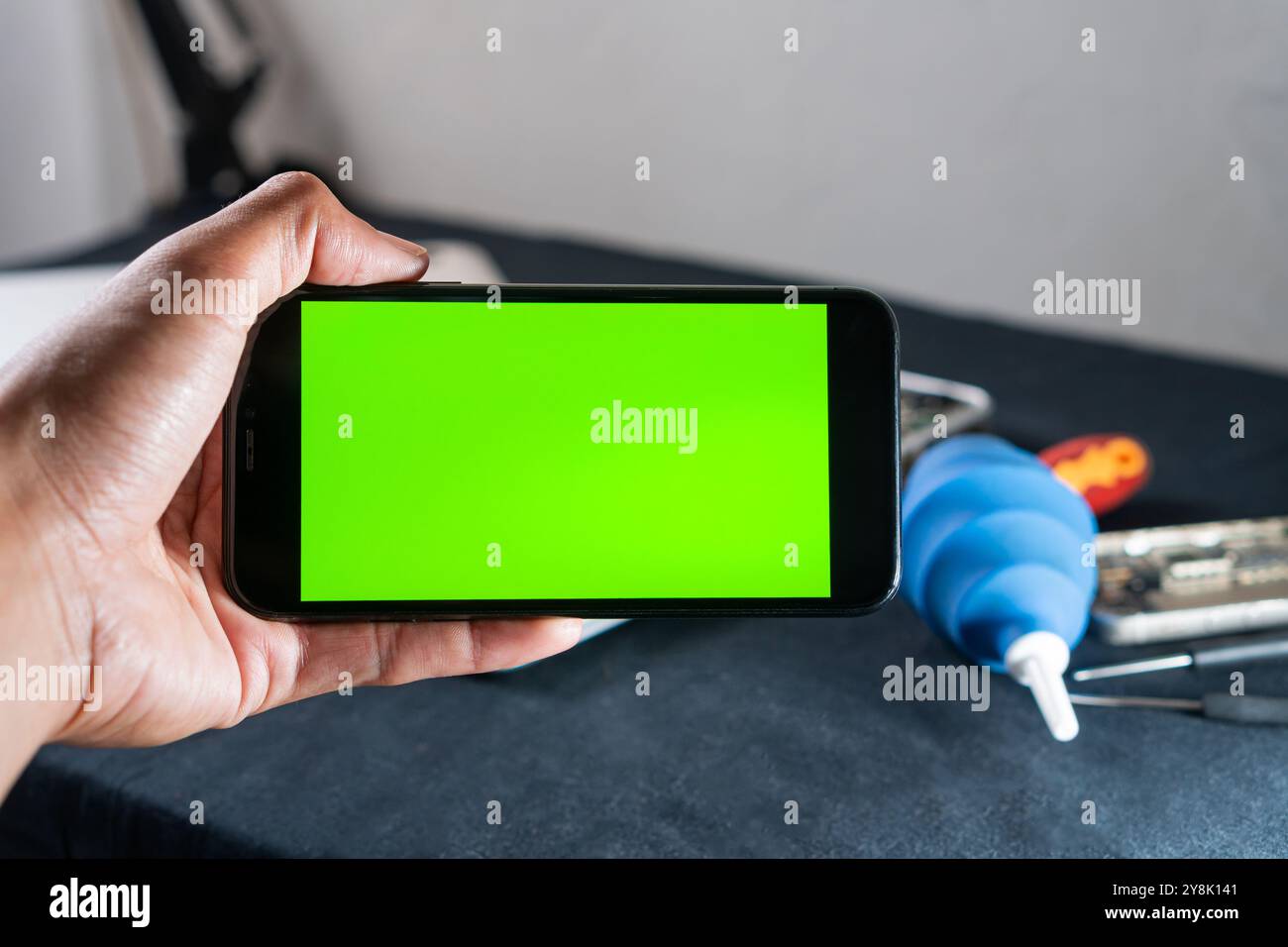 Une personne tenant un téléphone intelligent avec un écran vert vif, entouré de divers objets sur une table, y compris une seringue à ampoule bleue et d'autres outils. Th Banque D'Images