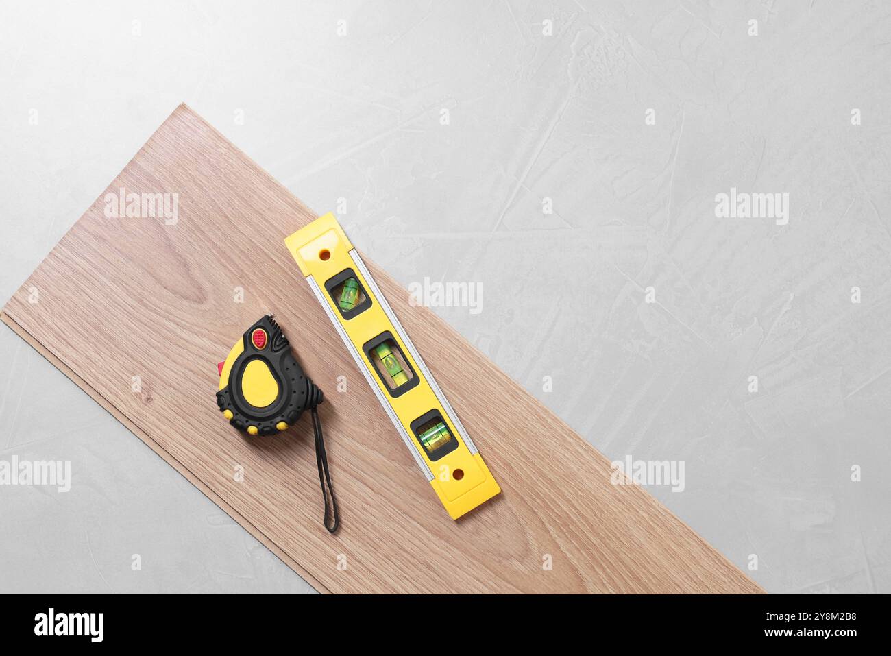 Différents outils de mesure et pièce de revêtement de sol stratifié sur surface texturée grise, vue de dessus. Espace pour le texte Banque D'Images