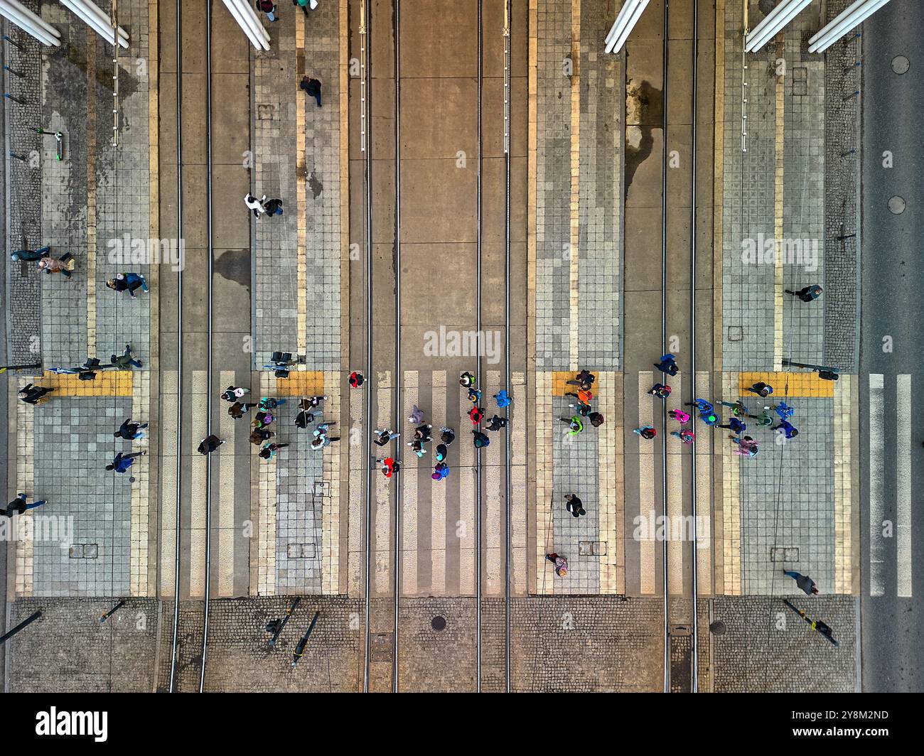 Vue de haut en bas de piétons traversant des voies de tramway dans un cadre urbain animé à Łódź, Pologne, capturée d'en haut avec des motifs géométriques de trottoirs an Banque D'Images