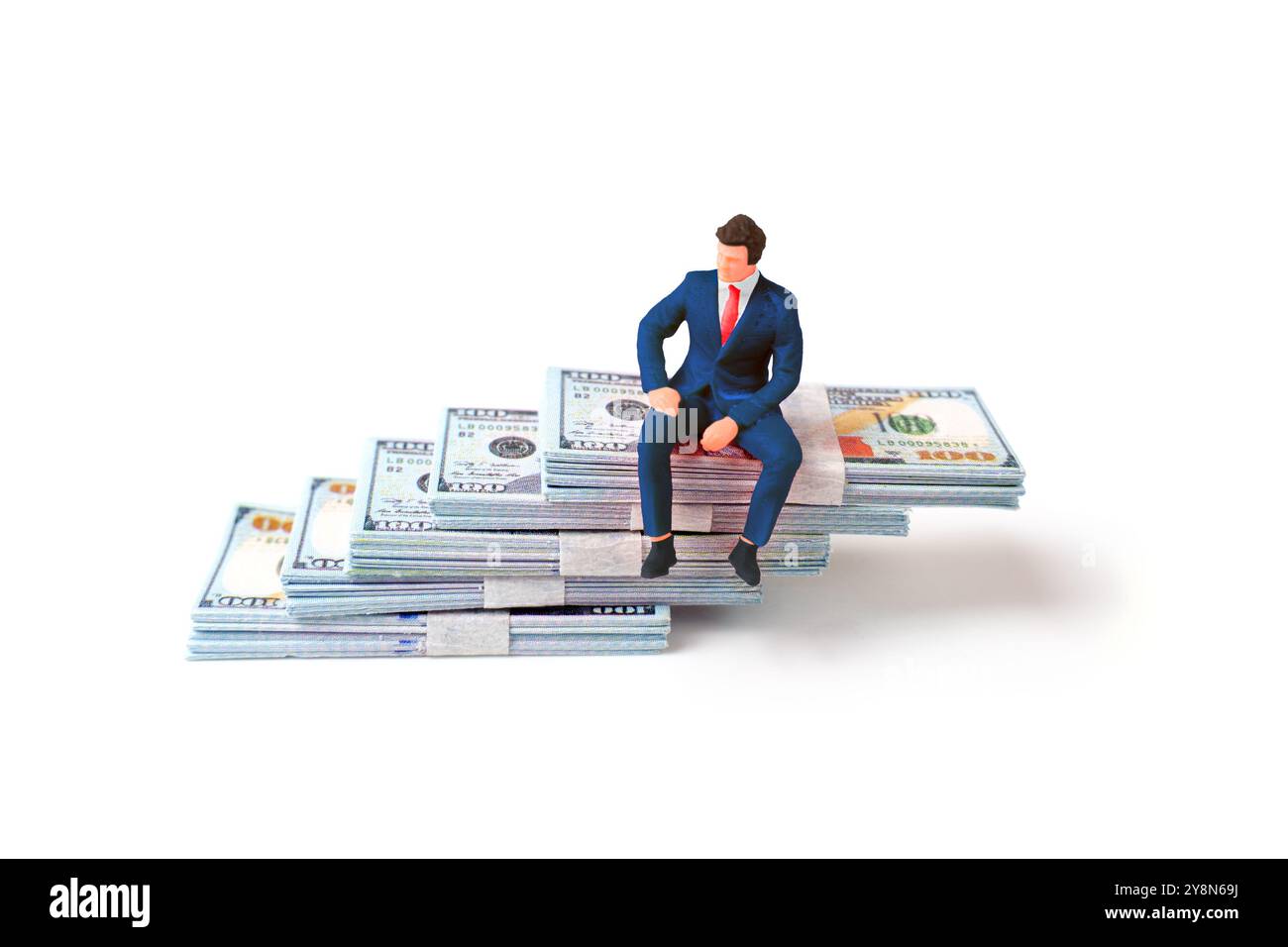 Figurine miniature d'un homme d'affaires assis sur des piles de liquidités, représentant la richesse, la finance et les concepts d'investissement. Banque D'Images