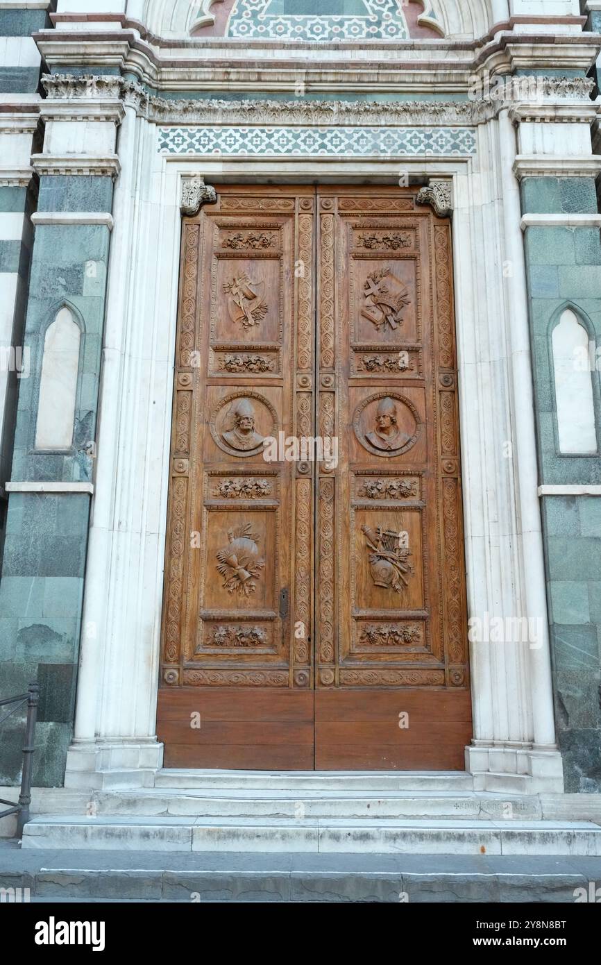 Le portail gothique orné et les portes en bois encadrés par des panneaux de marbre polychrome complexes sur la façade extérieure de la cathédrale de Florence, en Italie. Banque D'Images