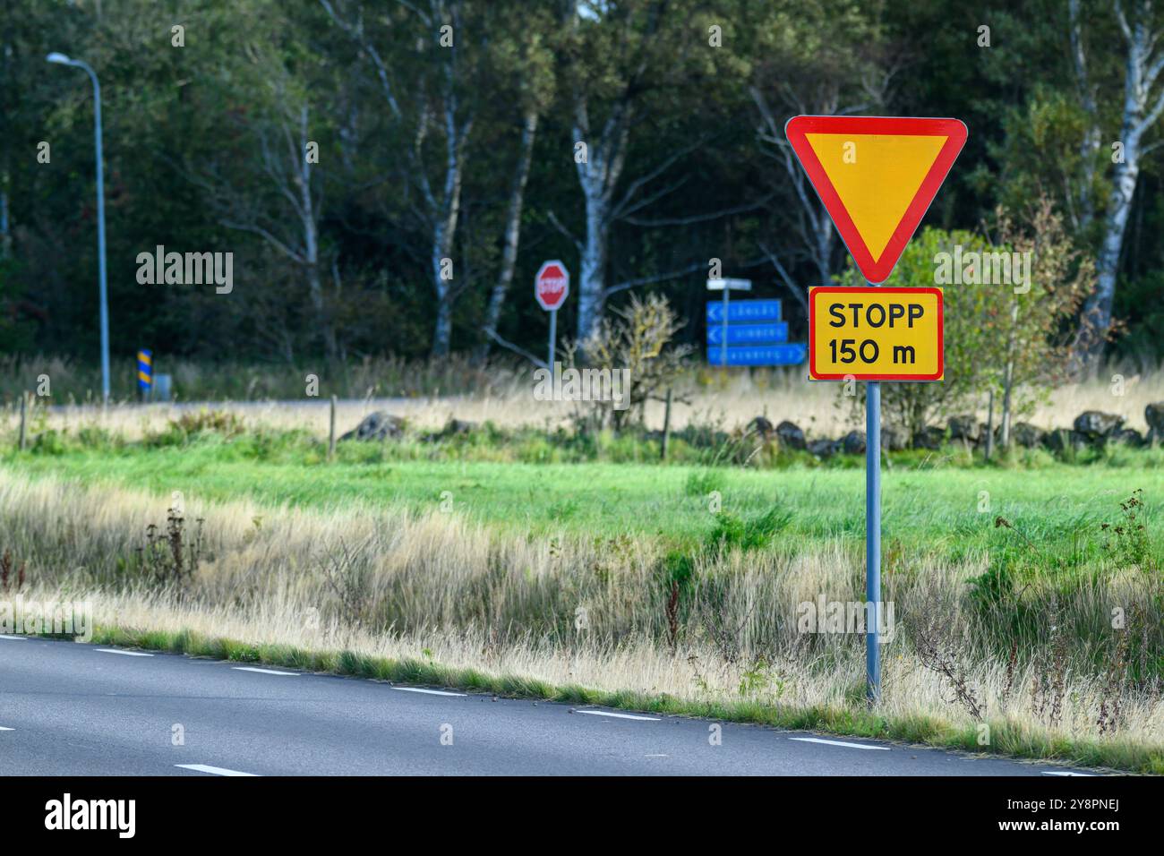 Un panneau d'avertissement triangulaire avertit les conducteurs d'un arrêt devant eux, positionné sur une route rurale bordée d'herbe et d'arbres. Le temps clair améliore v Banque D'Images
