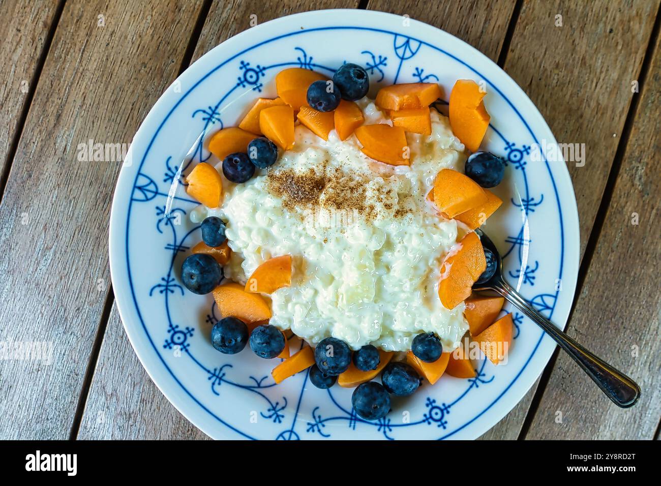 Un repas simple mais délicieux pendant les chaudes journées d'été : du pudding de riz chaud à la cannelle, garni de fruits frais tels que des abricots, des myrtilles ou fraîchement préparés Banque D'Images