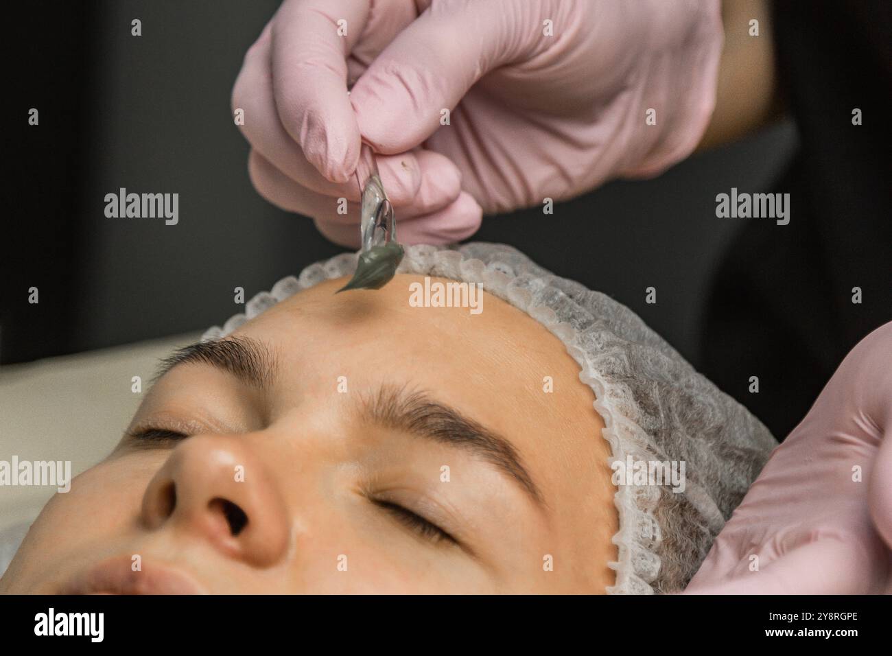 Le concept de cosmétologie. Gros plan d'une esthéticienne appliquant un masque vert avec un pinceau sur le visage d'une femme. Banque D'Images