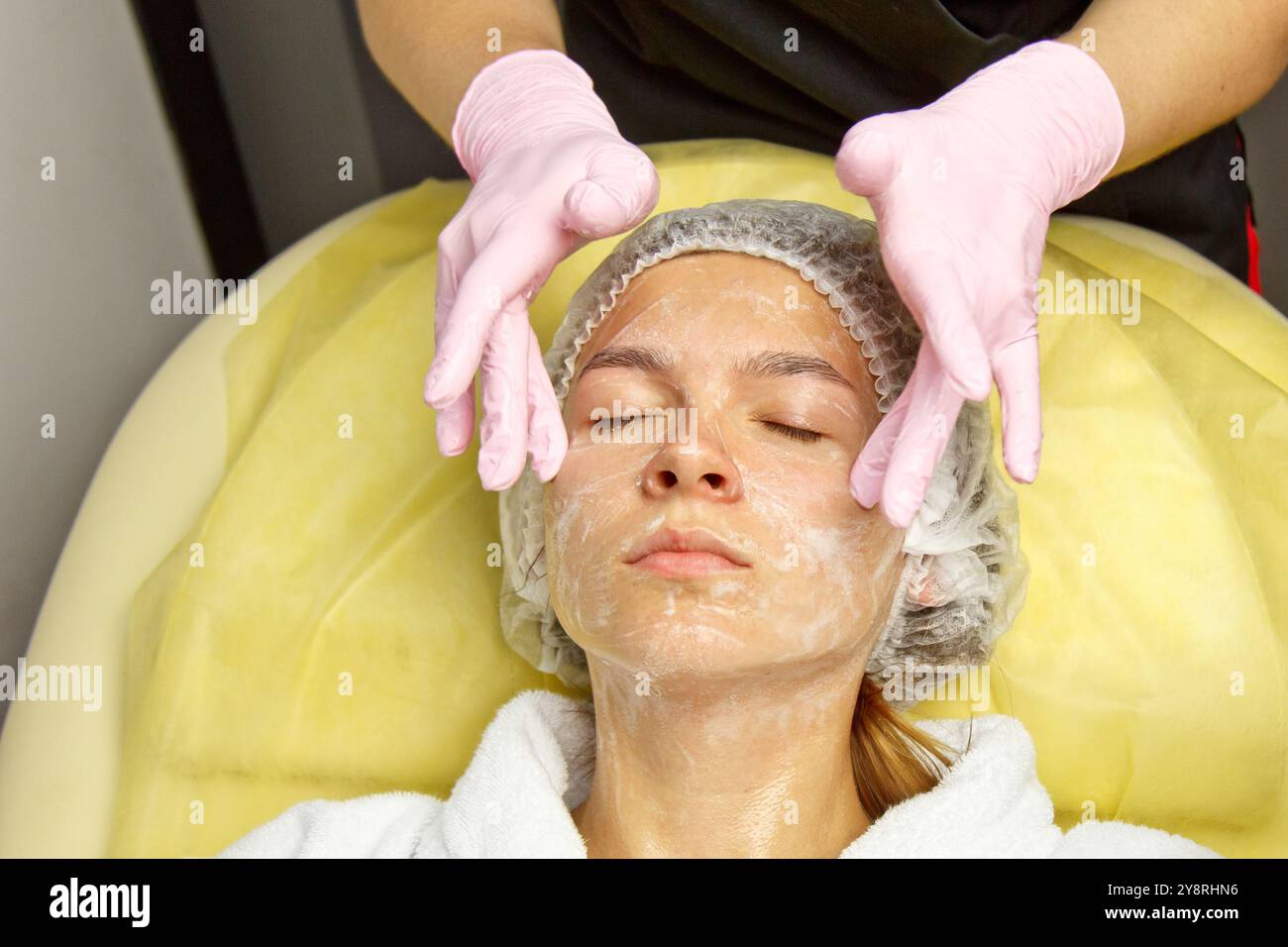 concept esthéticienne. Les mains d'un cosmétologue mettent de la crème sur le visage d'une femme. Esthéticienne applique une crème sur le visage de la fille. Banque D'Images