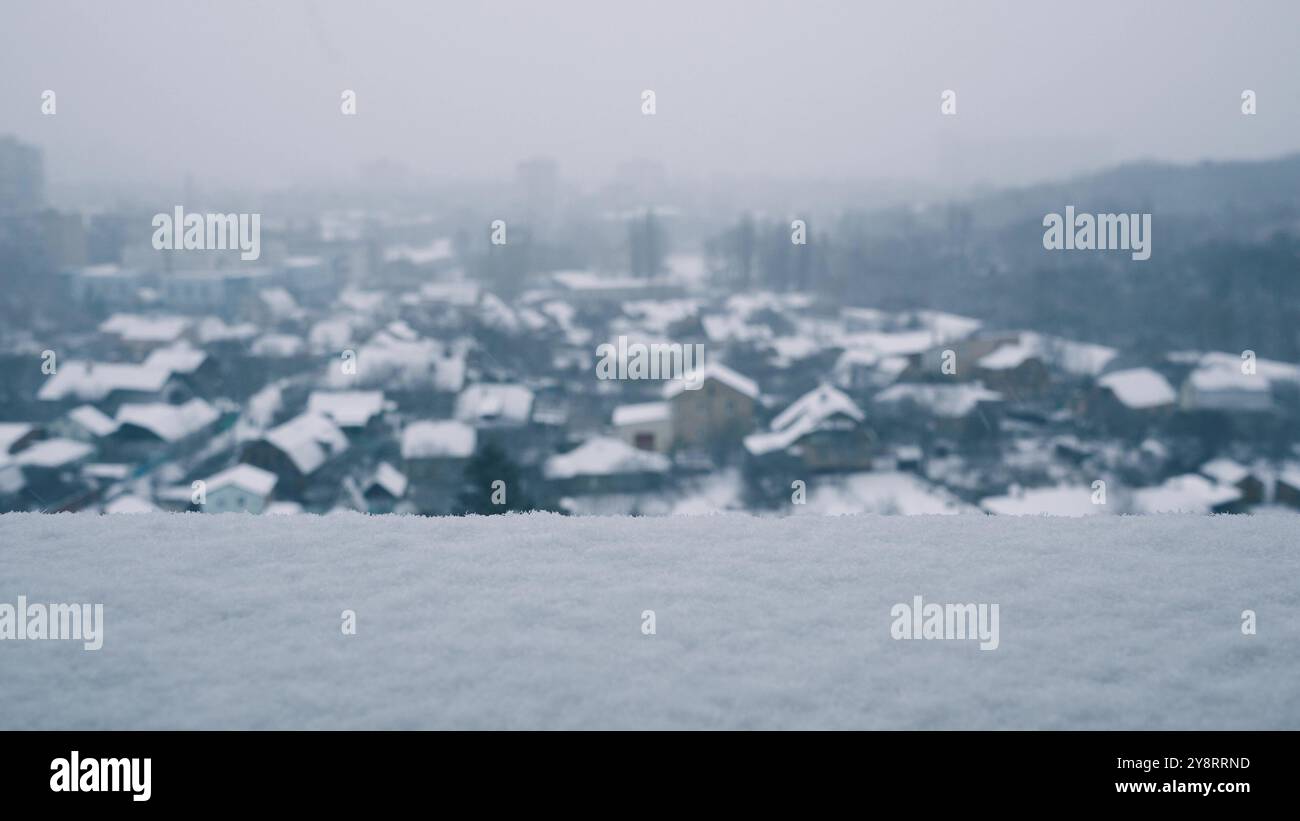 Une couche de neige blanche même gelée repose sur le rebord d'une fenêtre de grande hauteur par temps ensoleillé d'hiver. Les flocons de neige tourbillonnent et tombent sur le groun flou Banque D'Images