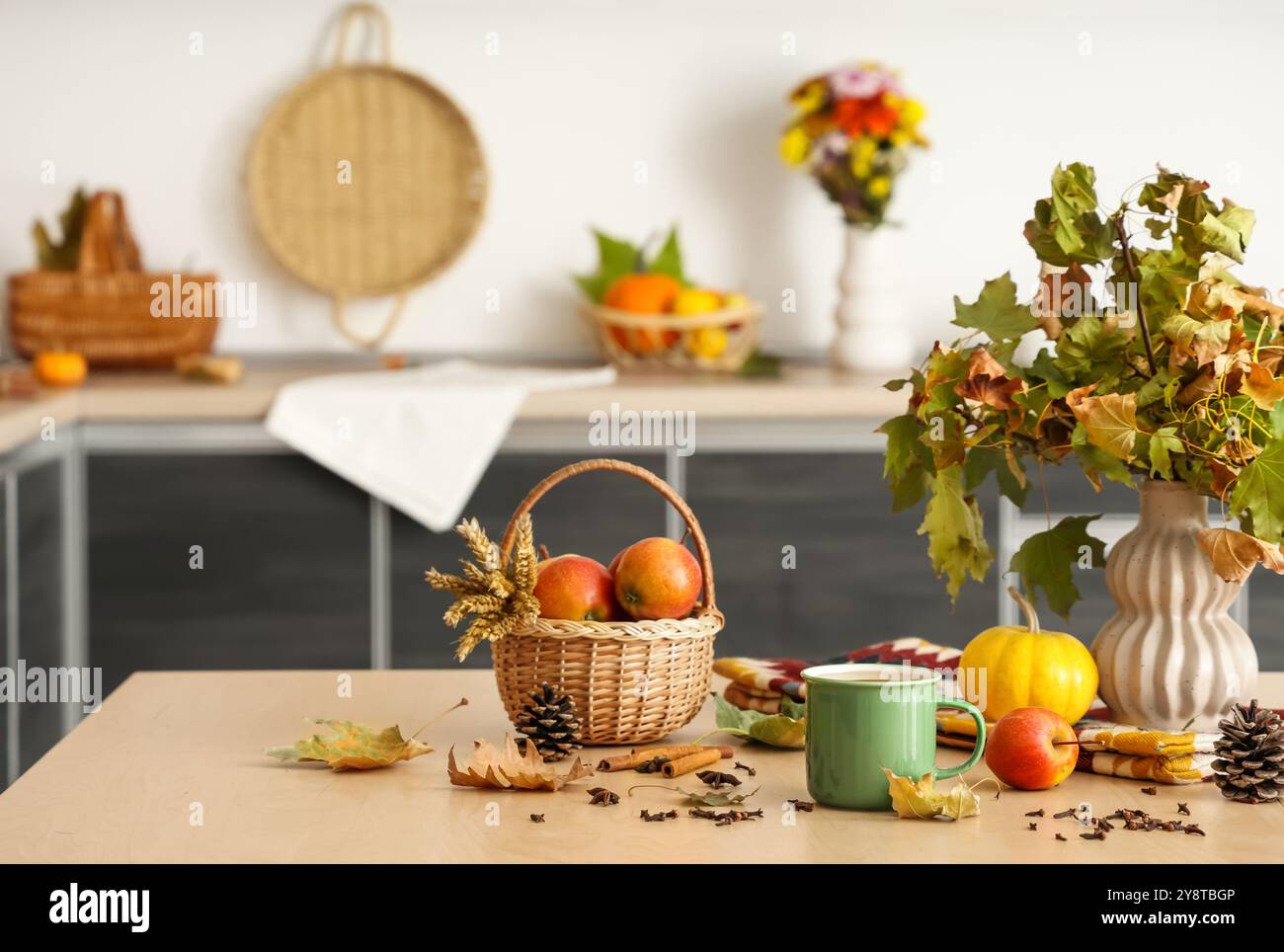 Vase avec des feuilles d'automne, tasse de thé vert chaud, panier avec des pommes et des épices sur la table dans la cuisine Banque D'Images