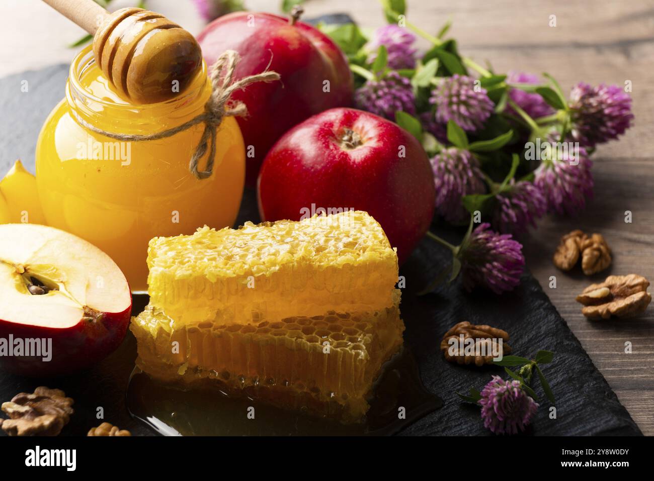 Pot Mason avec miel, balancier de miel, nid d'abeille, pommes rouges et noix sur la table de cuisine Banque D'Images