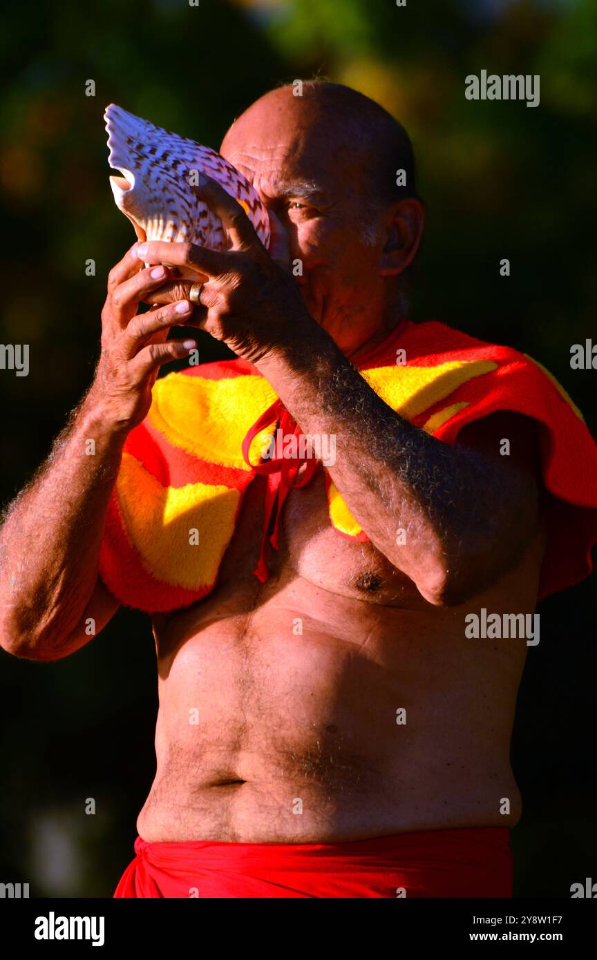 Un homme vêtu de vêtements hawaïens traditionnels souffle à travers une coquille de conque et accueille les invités à Waikiki Beach, Hawaï Banque D'Images