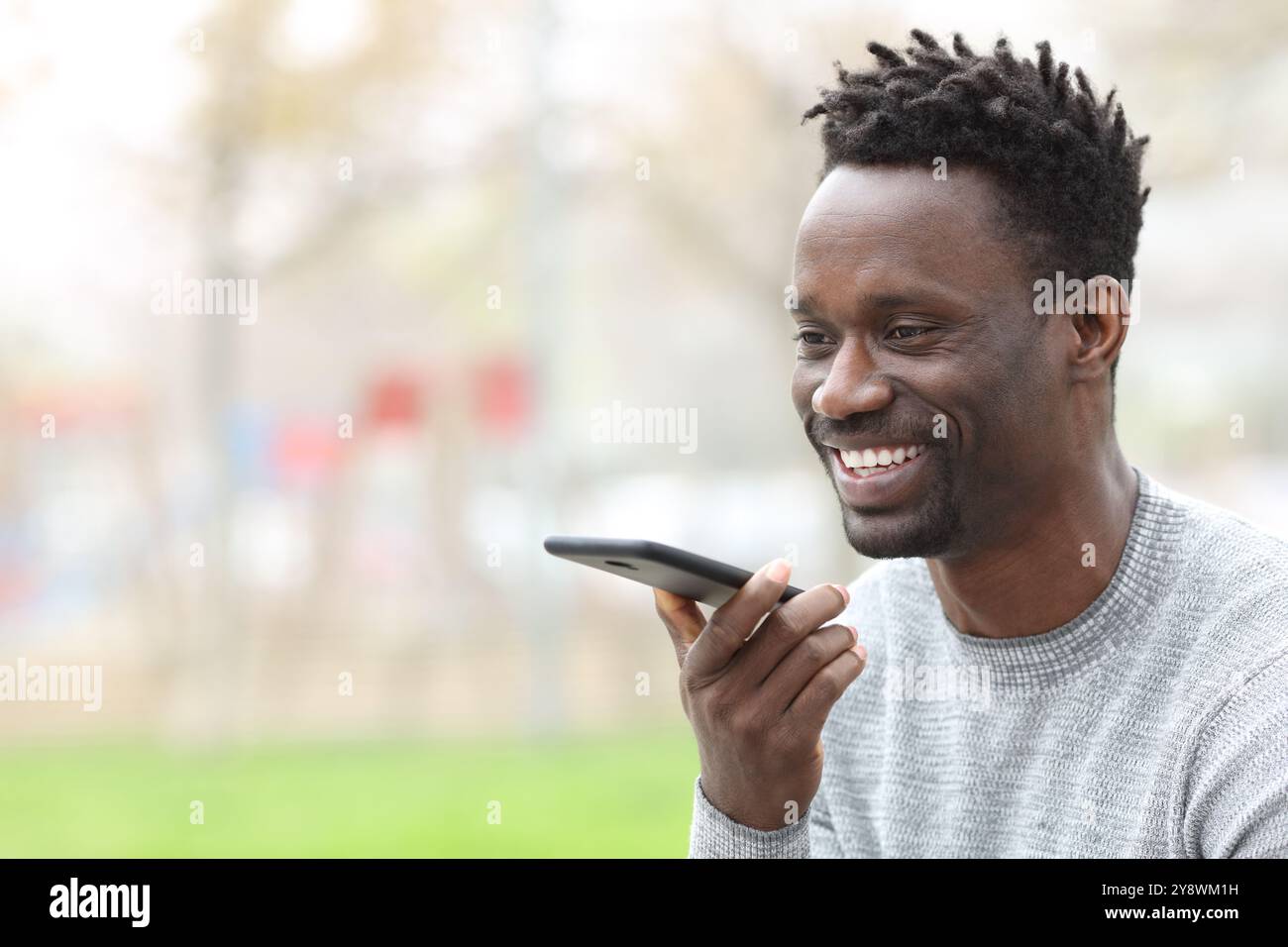 Homme noir heureux dictant un message sur le téléphone portable dans la rue Banque D'Images