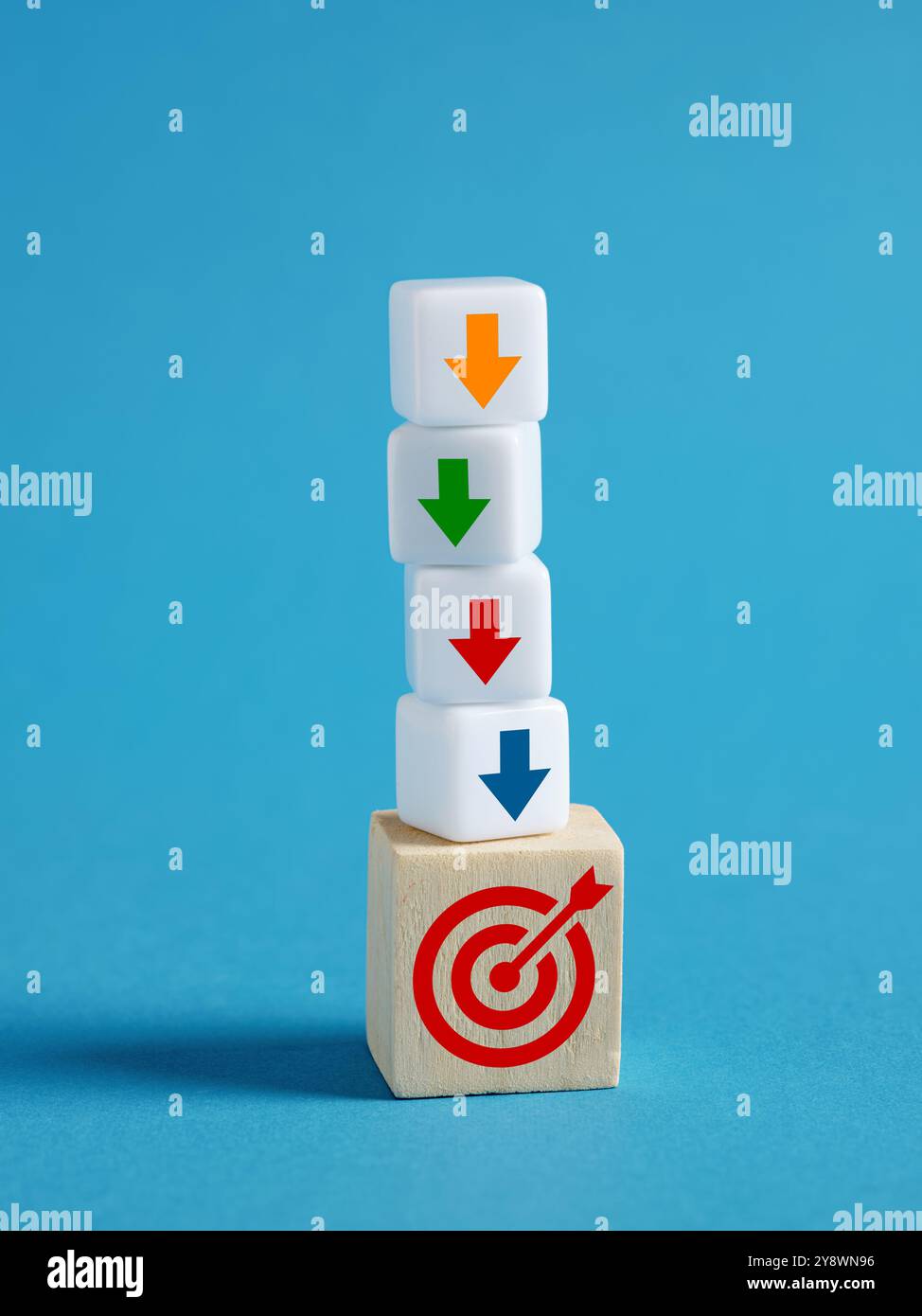 Pile de cubes affichant un symbole cible et des flèches pointant vers le bas, représentant une approche étape par étape pour se concentrer et atteindre les objectifs. Banque D'Images