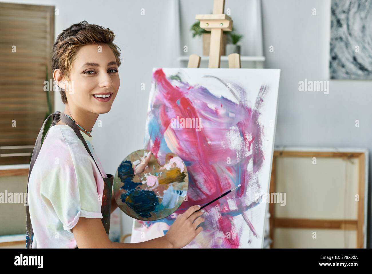 Une jeune femme peint joyeusement une œuvre d'art colorée à la maison, mettant en valeur sa passion pour l'art et la créativité. Banque D'Images
