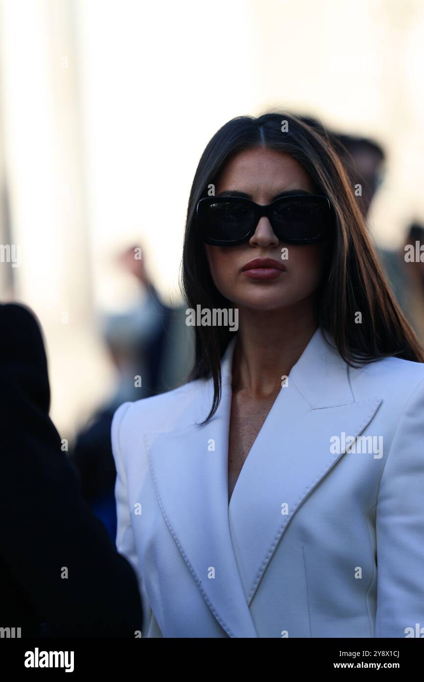 Une invitée portant un long manteau blanc classique et un petit sac à main pochette en noir de Chanel au salon Elie Saab pour Paris Fashion week SS25 Banque D'Images