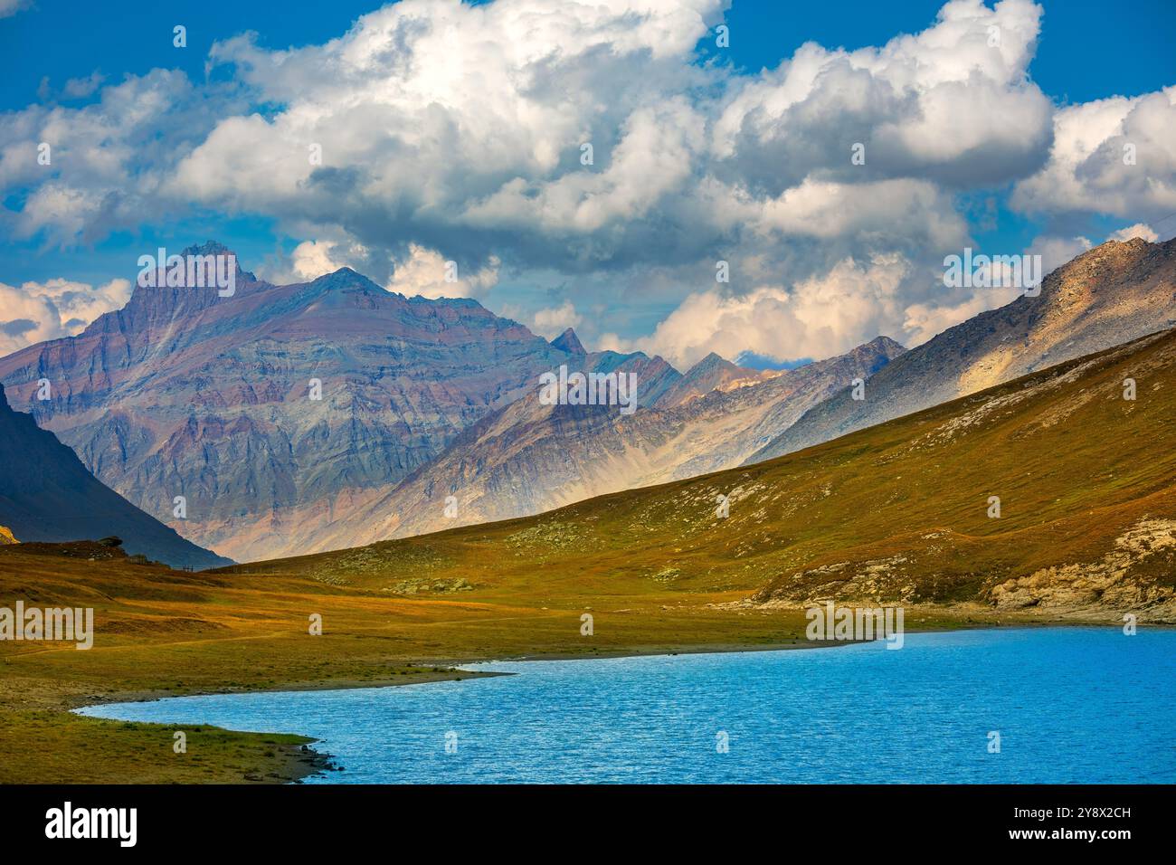 Vue sur le petit lac alpin et les montagnes sous beau ciel bleu avec des nuages blancs dans la vallée d'Aoste, Italie. Banque D'Images