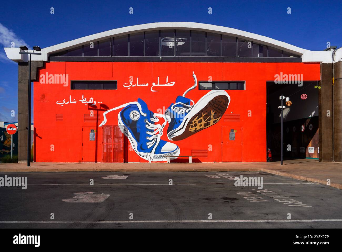 Un bâtiment rouge éclatant orné d'une grande murale de baskets bleues sur un ciel bleu clair dans le centre commercial O'village à casablanca Banque D'Images