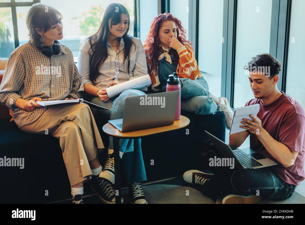 Un groupe diversifié d'étudiants collégiaux dans une bibliothèque travaillant ensemble sur un projet d'étude, illustrant le travail d'équipe et la collaboration. Banque D'Images
