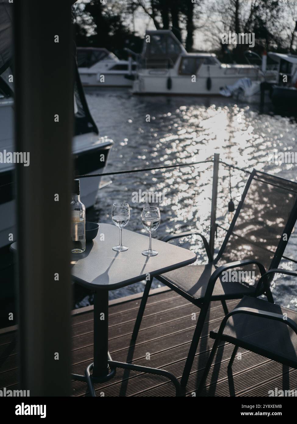 Une bouteille de vin blanc et deux verres sur un bateau maison moderne avec des eaux calmes et du soleil avec des lumières de fées et des bateaux en arrière-plan Banque D'Images
