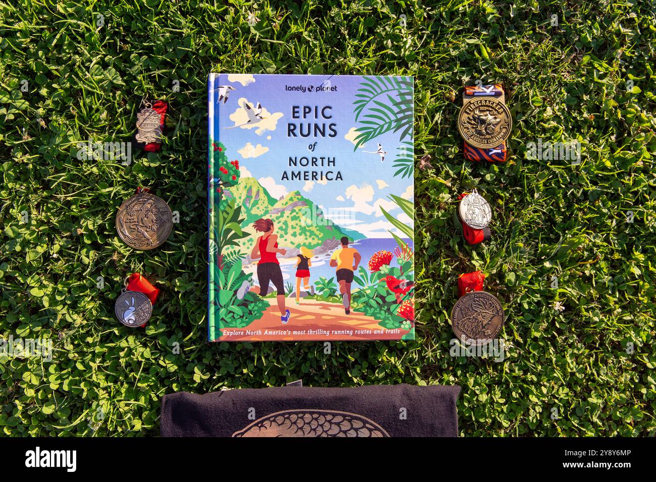 Lonley Planet, livre Epic Runs of North America sur une pelouse en herbe. À côté du livre se trouvent des médailles de course du Firecracker 10k, un chapitre vedette Banque D'Images