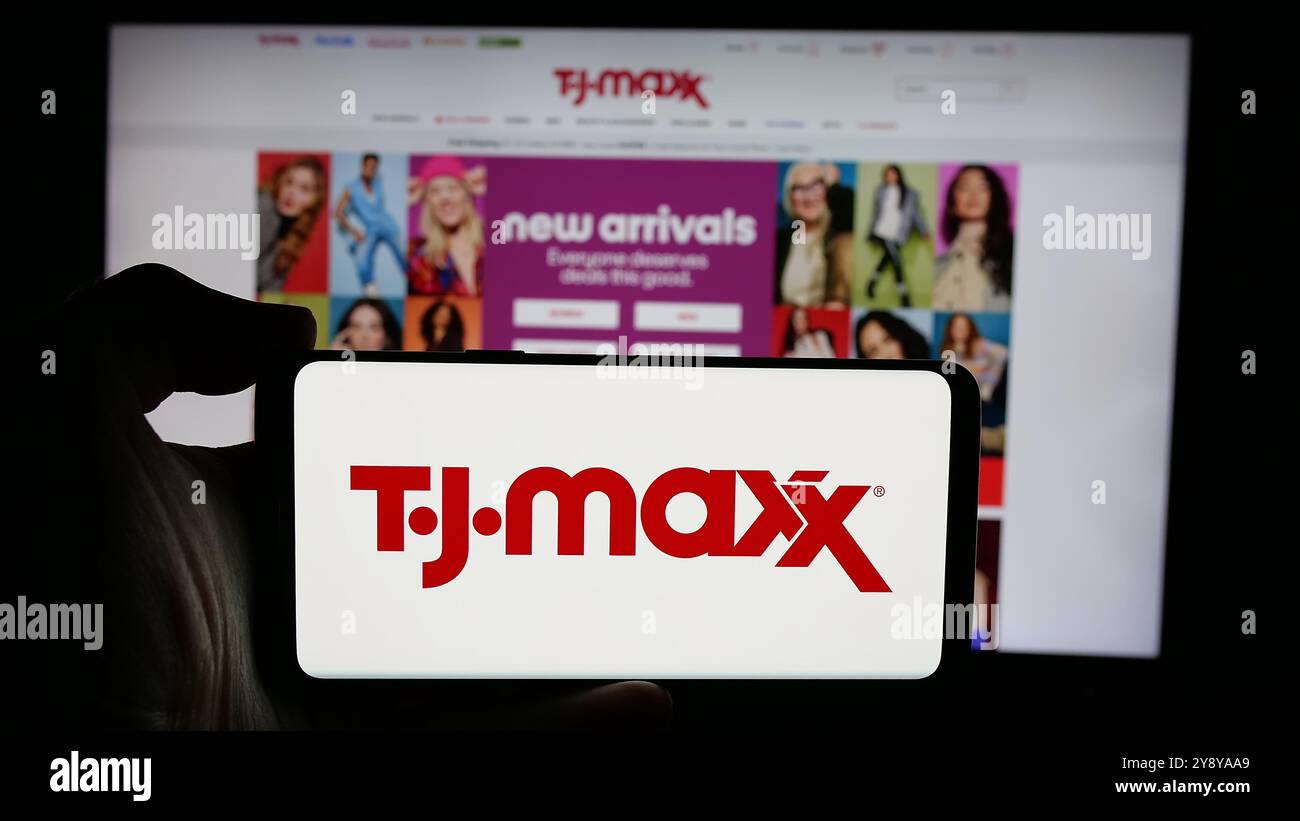 Personne tenant le téléphone portable avec le logo de la société américaine de magasin à rabais TJ Maxx sur l'écran en face de la page Web. Concentrez-vous sur l'affichage du téléphone. Banque D'Images
