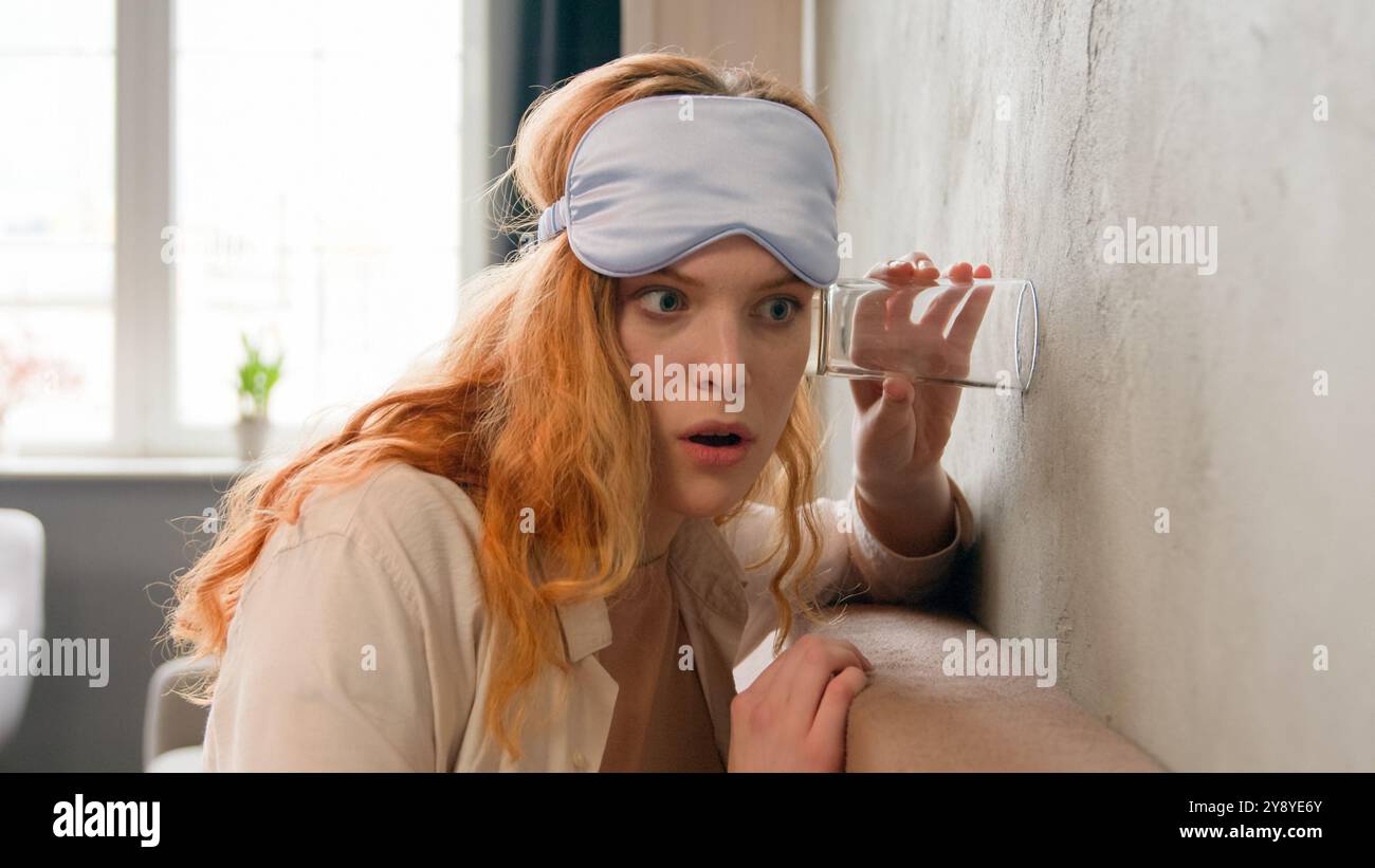 Fille en colère choquée penchée au mur dans la chambre à coucher tôt le matin curieuse femme caucasienne entendant un voisin bruyant en utilisant des voisins écoutant du verre Banque D'Images