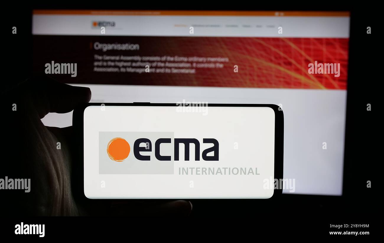 Personne tenant le téléphone portable avec le logo de l'organisation de normalisation Ecma International sur l'écran en face de la page Web. Concentrez-vous sur l'affichage du téléphone. Banque D'Images