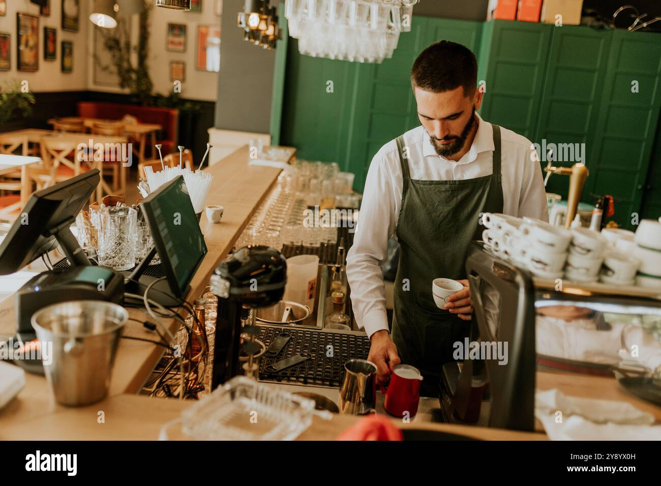 Dans un café chaleureux et accueillant, un barista dévoué verse habilement du lait dans une tasse à café, créant une expérience délicieuse pour les clients. Banque D'Images