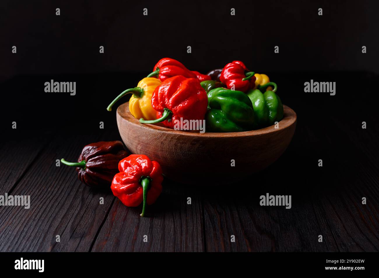 Poivrons habanero multicolores mûrs (capsicum chinense) dans un bol en bois sur une table rustique. Les poivrons mexicains très chauds se rapprochent Banque D'Images
