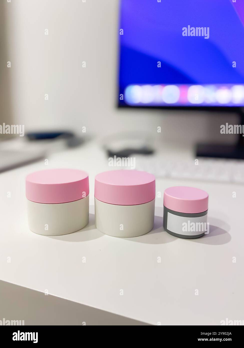 Configuration de bureau minimaliste avec trois pots de soins de la peau avec couvercles roses, parfaitement alignés sur un fond de technologie moderne. Copier l'espace. Élégant Banque D'Images