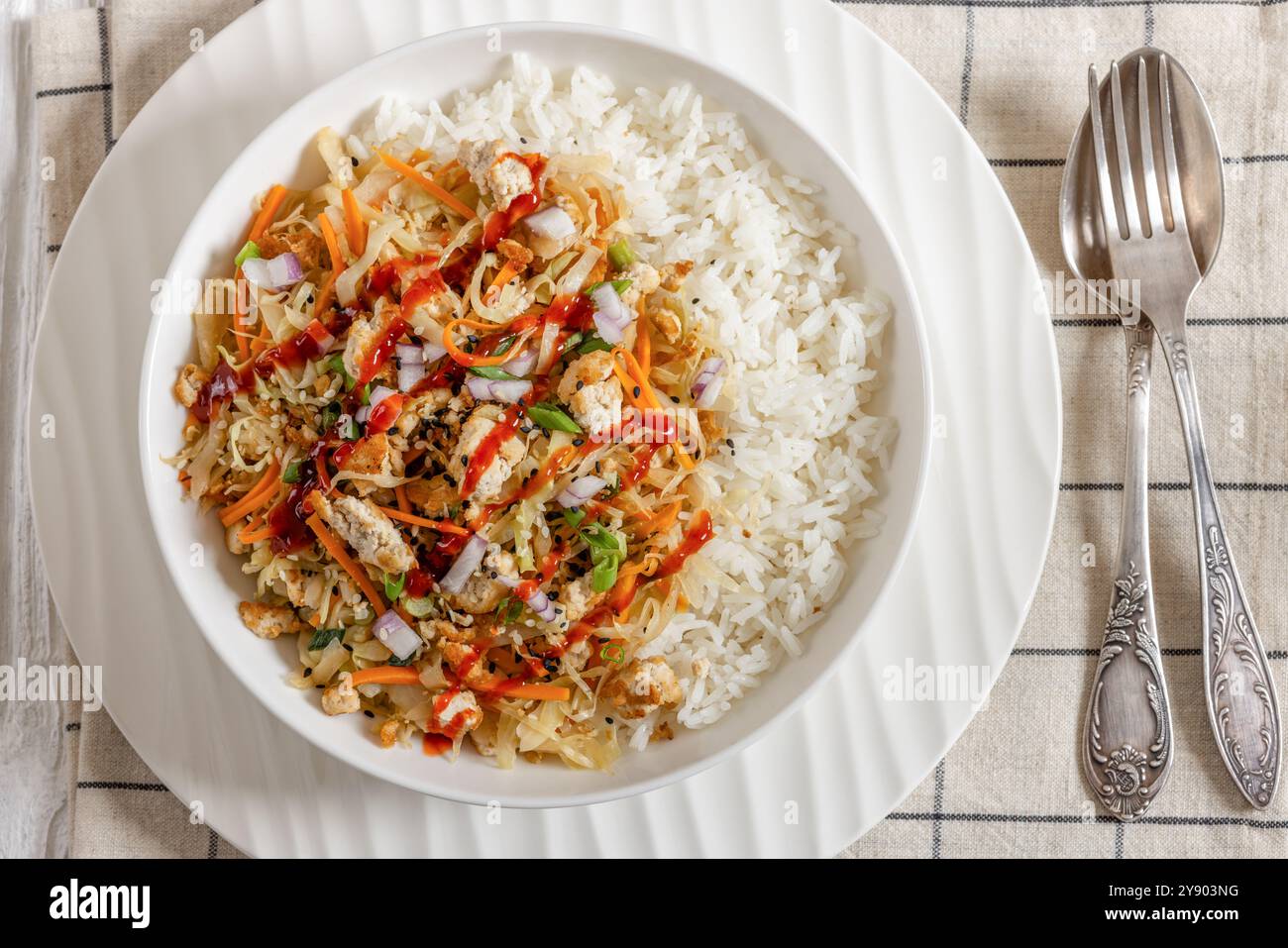 roulé aux œufs de tofu, chou sautés, tofu émietté assaisonné servi dans une sauce sucrée et salée servie sur du riz dans un bol sur une table en bois blanc avec fourchette Banque D'Images
