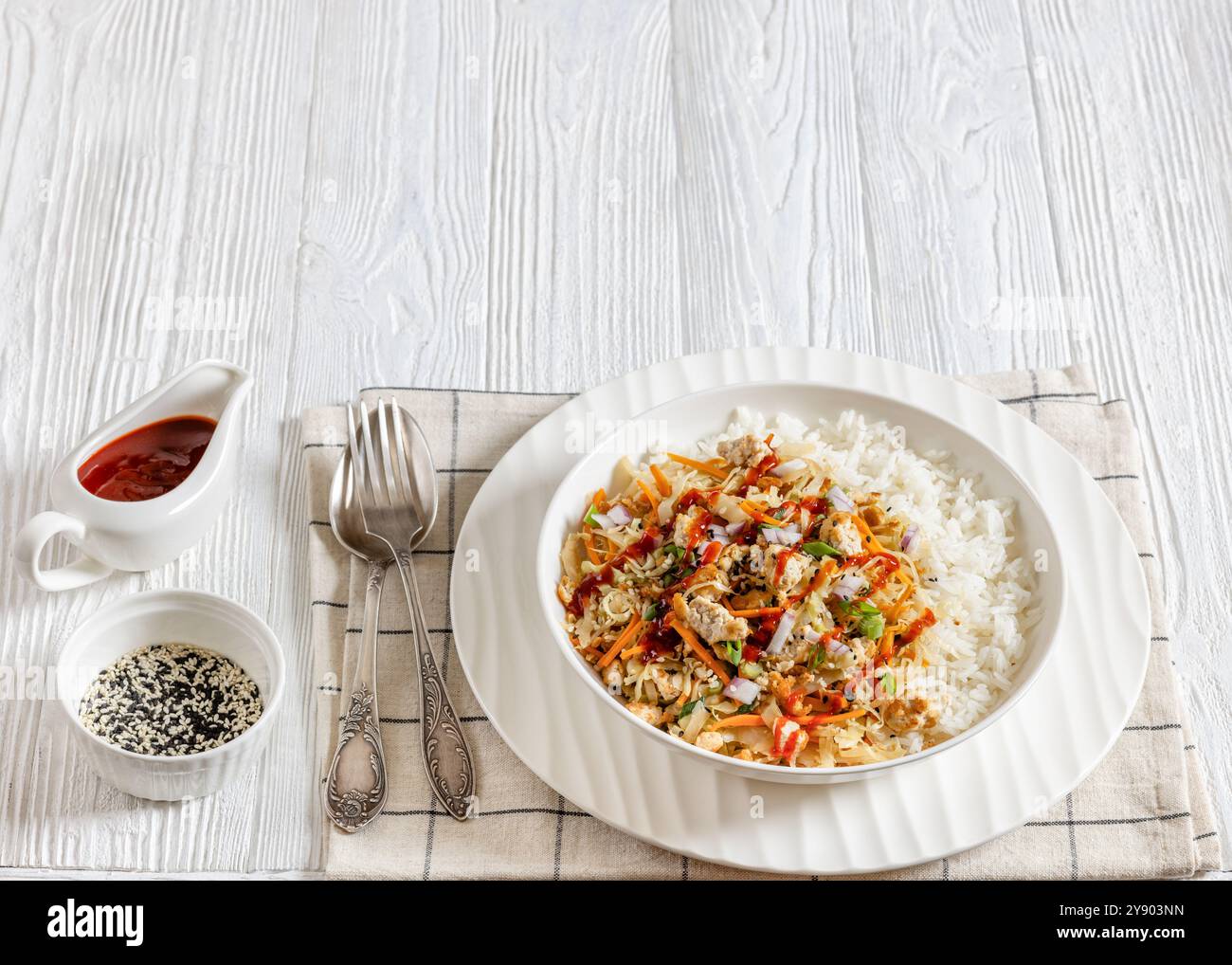 roulé aux œufs de tofu, chou sautés, tofu émietté assaisonné servi dans une sauce sucrée et salée servie sur du riz dans un bol sur une table en bois blanc avec fourchette Banque D'Images