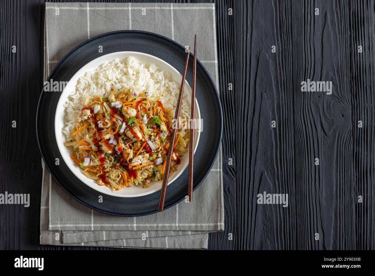 roulé aux œufs de tofu, chou sautés, tofu émietté assaisonné servi dans une sauce sucrée et salée servie sur du riz dans un bol avec des baguettes sur du ta en bois noir Banque D'Images