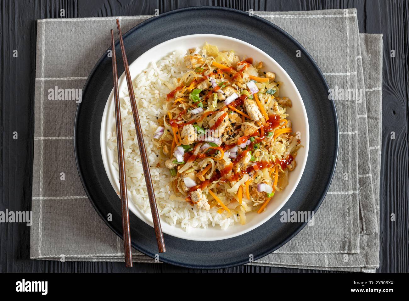 roulé aux œufs de tofu, chou sautés, tofu émietté assaisonné servi dans une sauce sucrée et salée servie sur du riz dans un bol avec des baguettes sur du ta en bois noir Banque D'Images