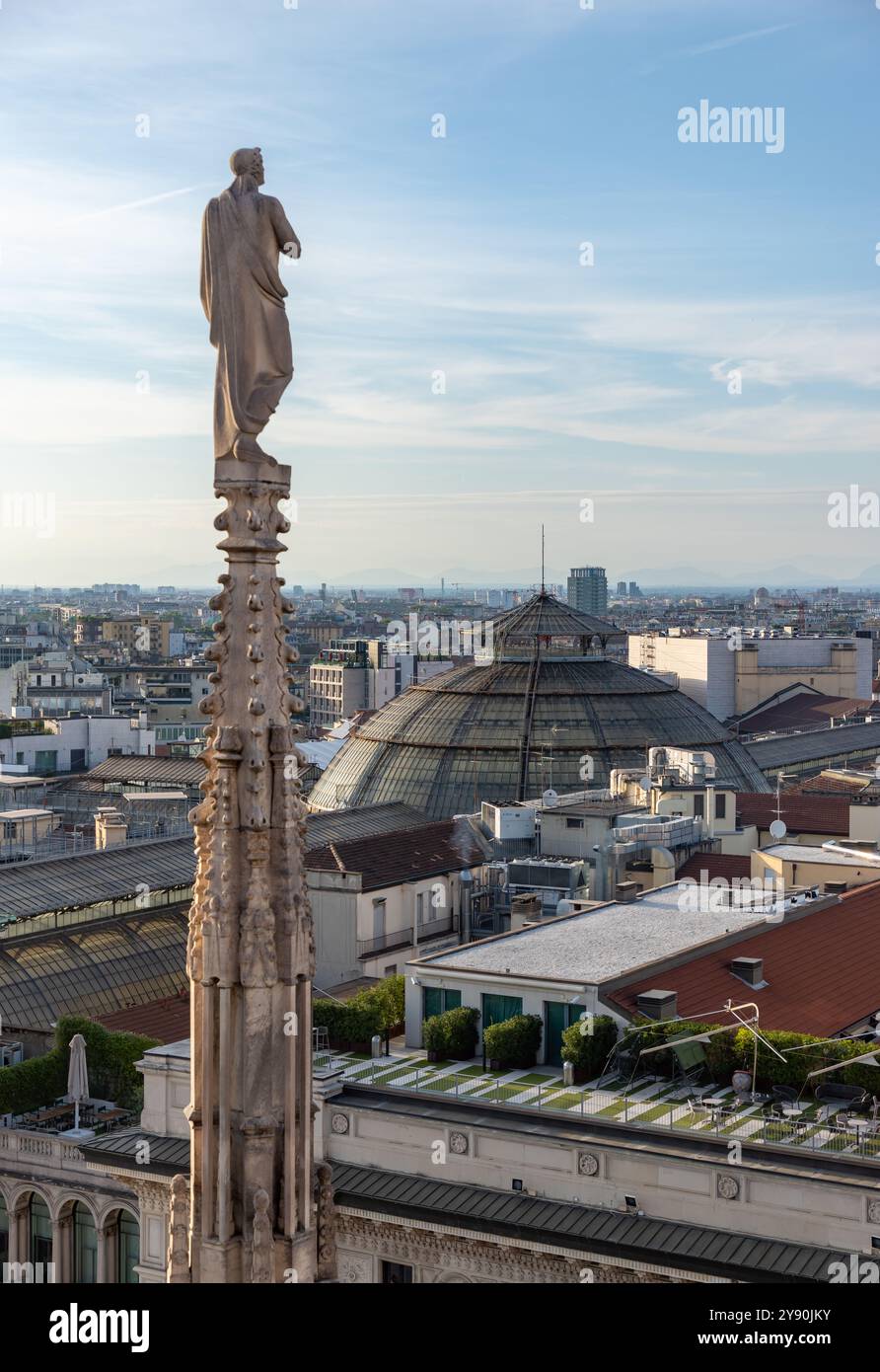 Photo d'une flèche et d'une statue du toit du Duomo di Milano ou de la cathédrale de Milan surplombant le toit de la Galleria Vittorio Emanuele II. Banque D'Images