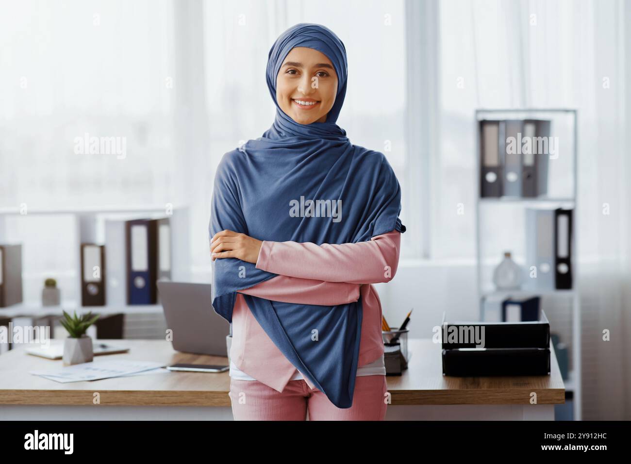 Femme d'affaires musulmane confiante debout avec les bras pliés près du lieu de travail au bureau Banque D'Images