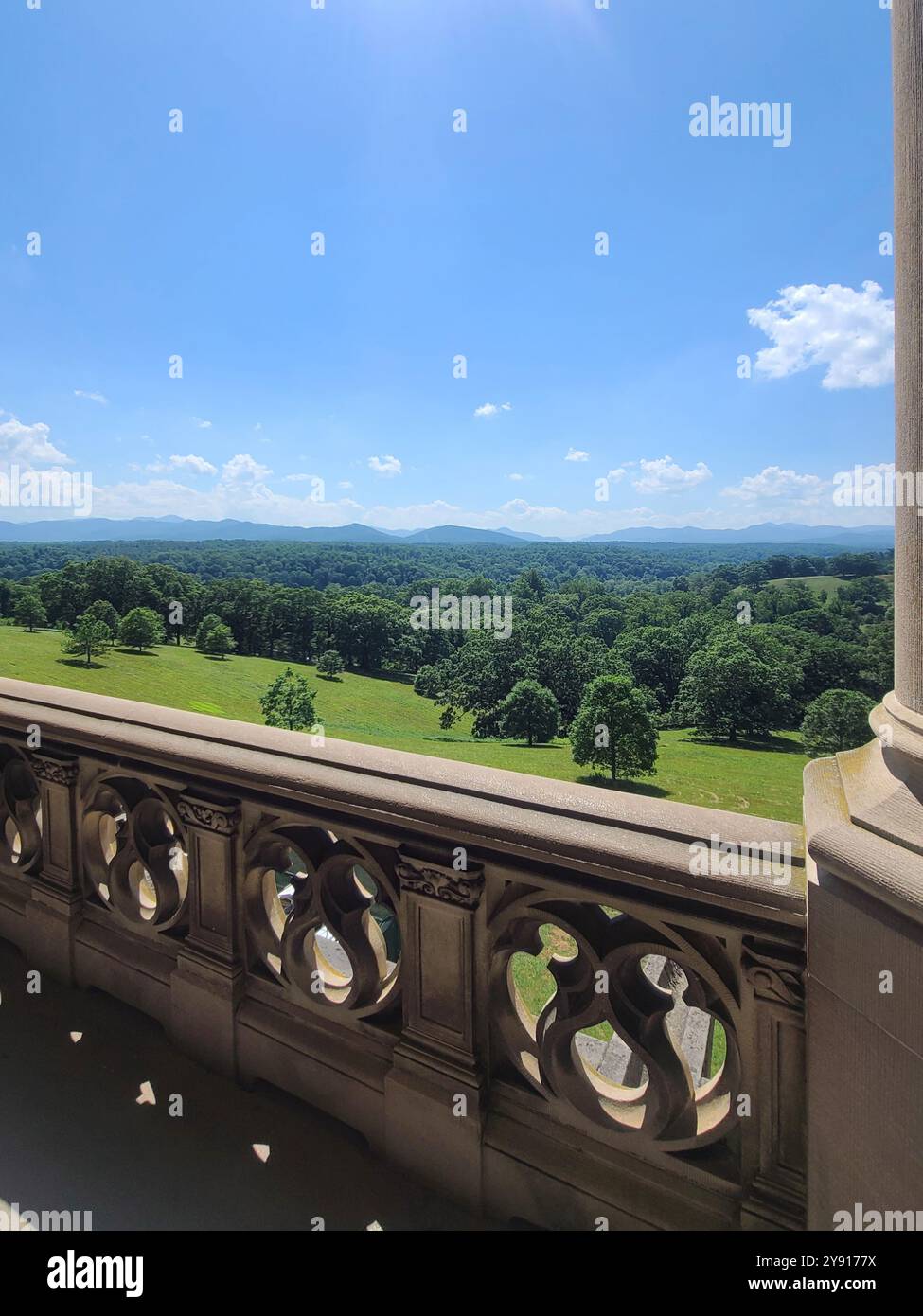 Vue panoramique depuis un balcon en pierre donnant sur un paysage verdoyant luxuriant avec des montagnes lointaines sous un ciel bleu clair. Banque D'Images