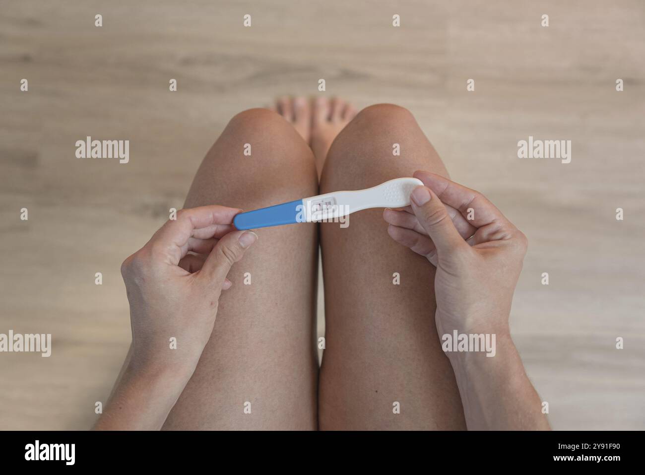 Une personne tient un test de grossesse positif au-dessus de ses genoux, image symbolique d'une nouvelle vie, plancher en bois Banque D'Images