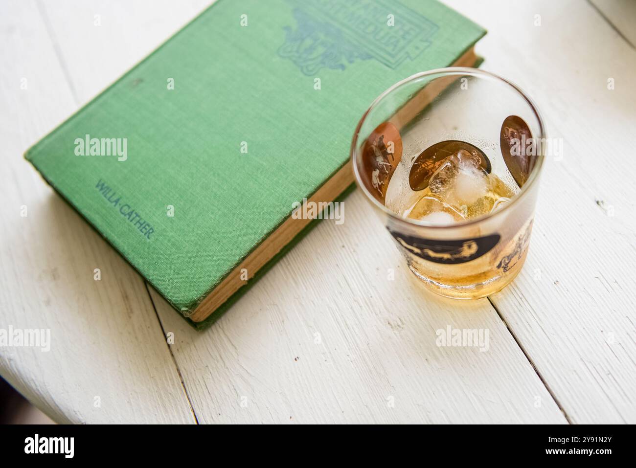 Photographie de whisky de scotch sur la boisson glacée de roches à côté d'un livre de Willa Cather sur le dessus d'une table. Banque D'Images