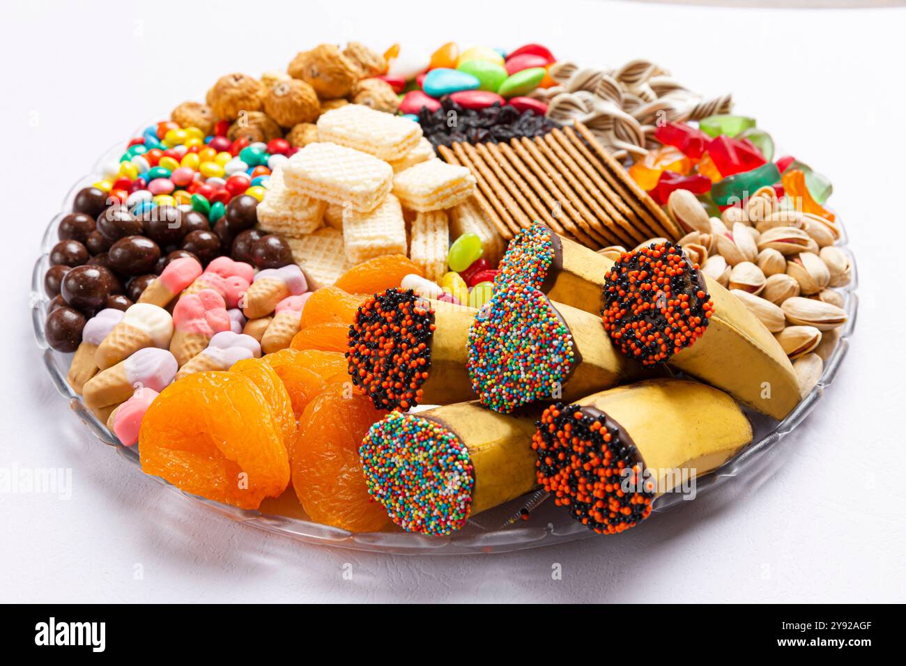 Un assortiment coloré de collations comprenant des fruits secs, des gaufrettes, des pistaches, des bonbons et des bananes décorées, idéal pour les fêtes ou les friandises festives Banque D'Images