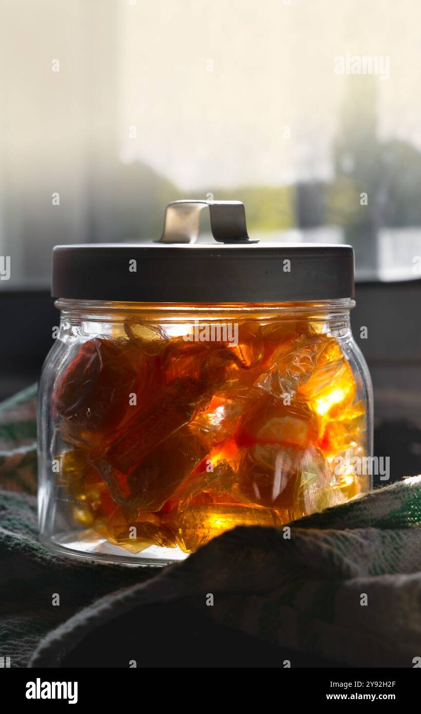 Un pot de bonbons au miel se trouve sur une table. Les bonbons sont dans une variété de formes et de tailles, et ils sont tous jaunes. Le pot est en verre et a un Banque D'Images