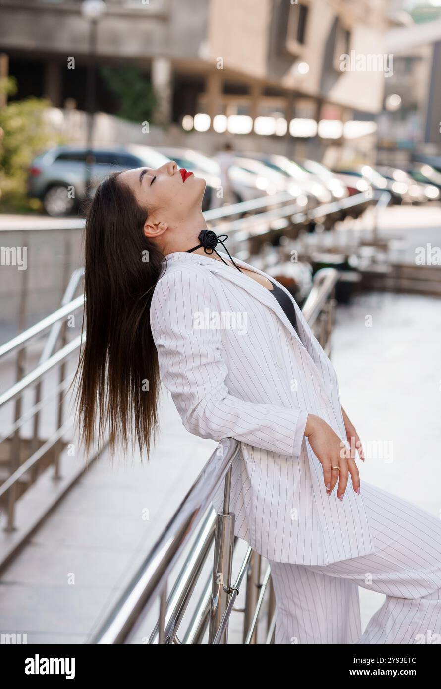 Femme élégante en costume rayé posant en toute confiance à l'extérieur. Banque D'Images