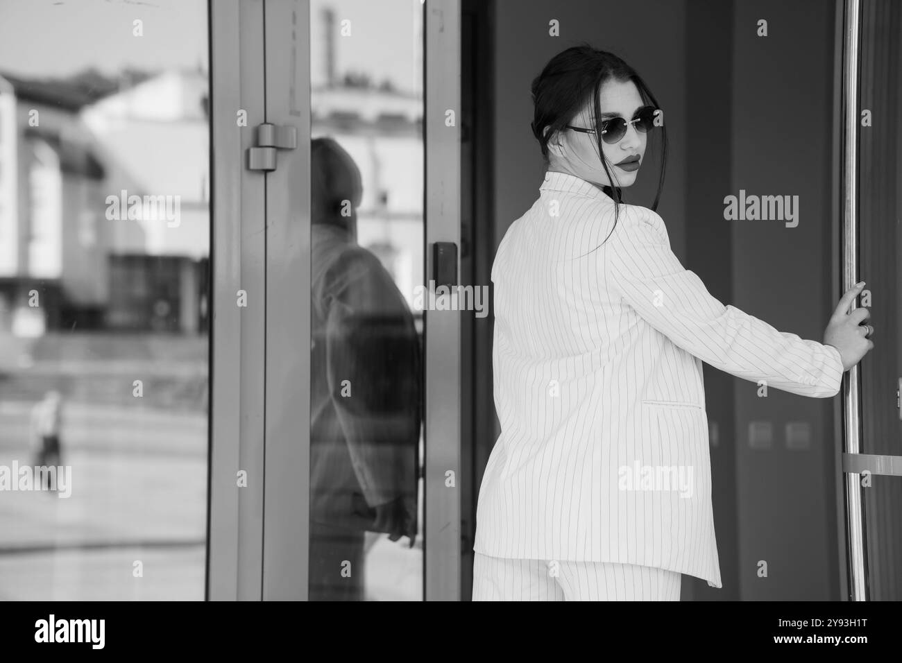 Femme d'affaires chic posant élégamment par la porte vitrée en noir et blanc. Banque D'Images