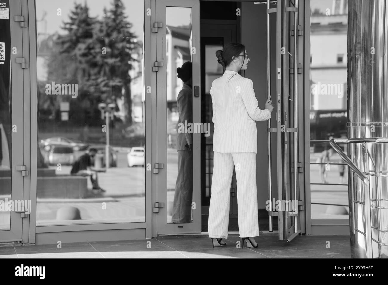 Femme d'affaires élégante sortant d'un bâtiment en verre moderne dans un costume élégant à fines rayures. Banque D'Images