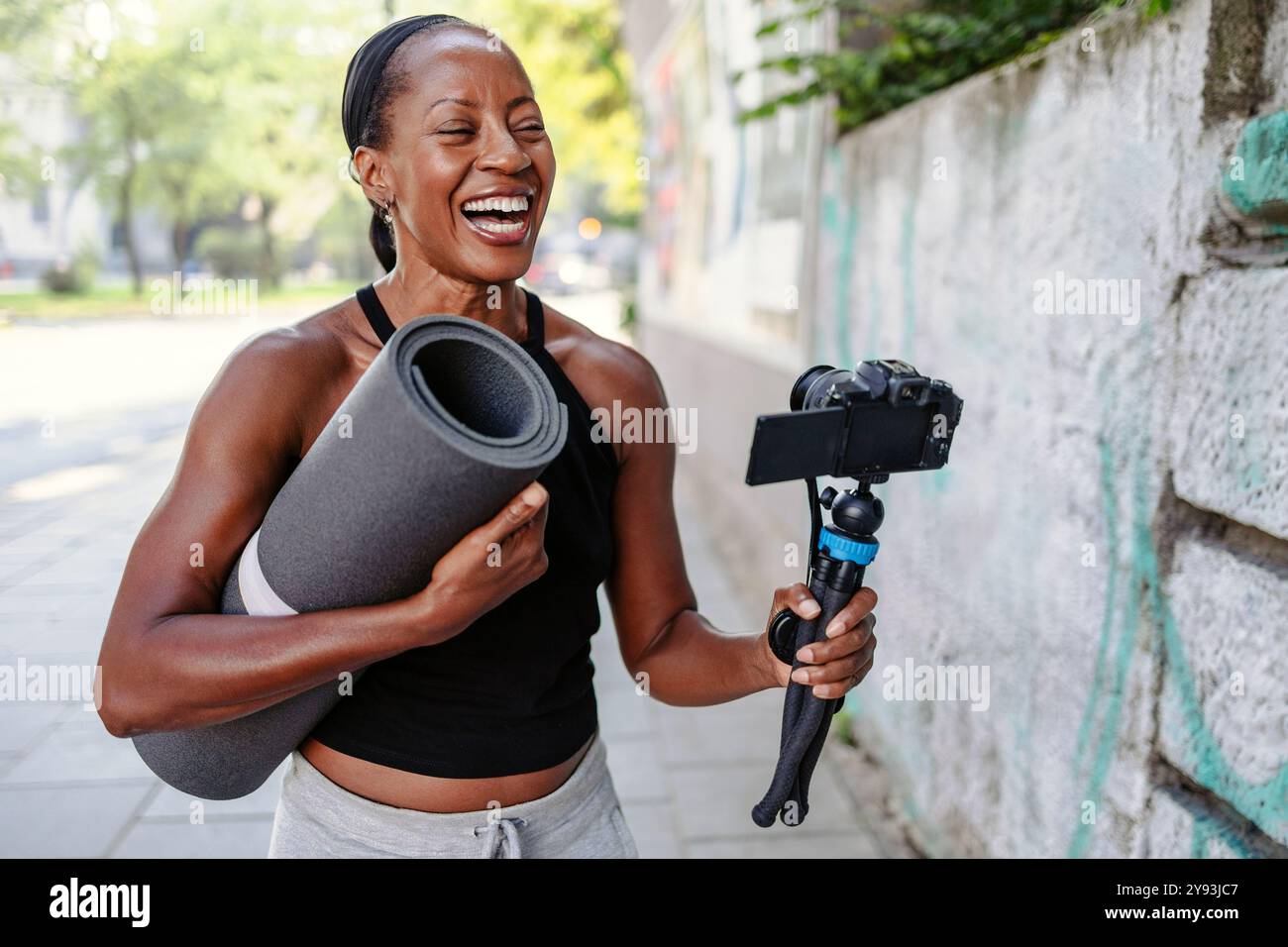 Vlogger sportive tenant son appareil photo et son tapis d'exercice dans la ville Banque D'Images