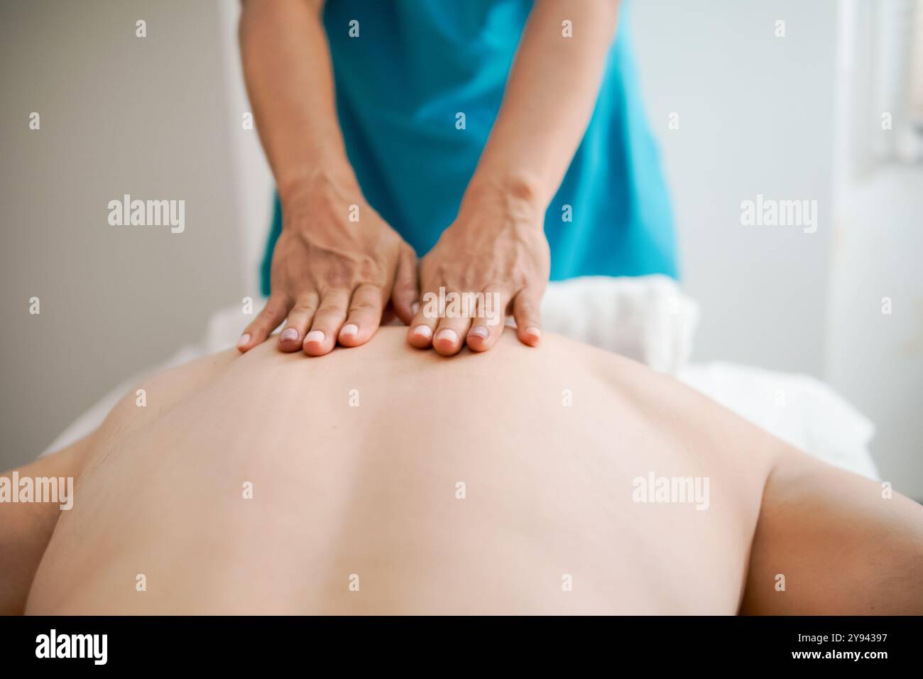 Massothérapeute féminine recadrée méconnaissable applique une pression avec ses mains sur le dos d'un client masculin qui reçoit un massage à domicile mentant Banque D'Images