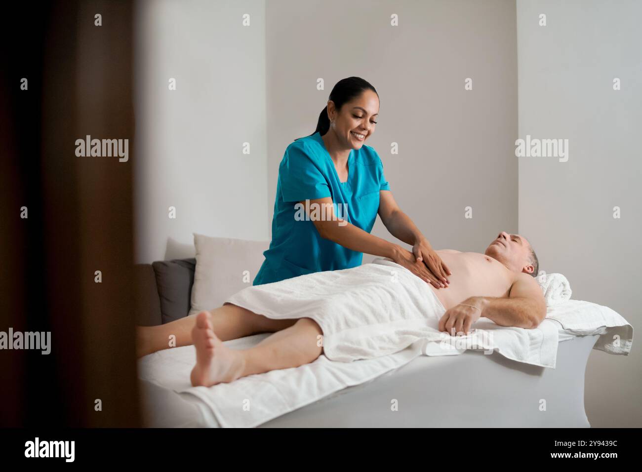 Une massothérapeute féminine fournit un massage abdominal relaxant à un client masculin allongé sur une table de massage à la maison. Banque D'Images