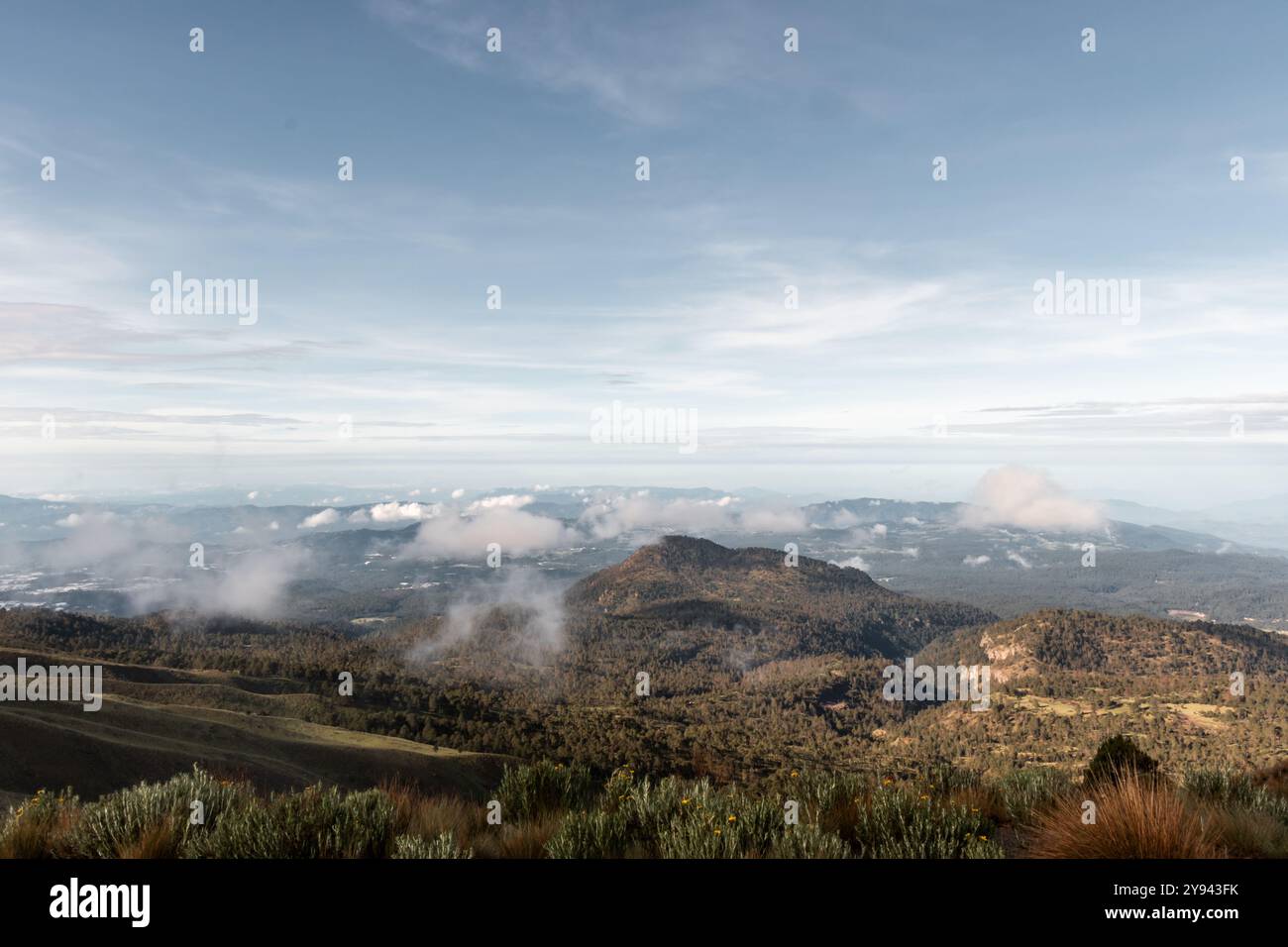 Vue panoramique sur un paysage magnifique avec des collines vallonnées, une végétation luxuriante et des montagnes enveloppées de nuages sous un vaste ciel. Banque D'Images
