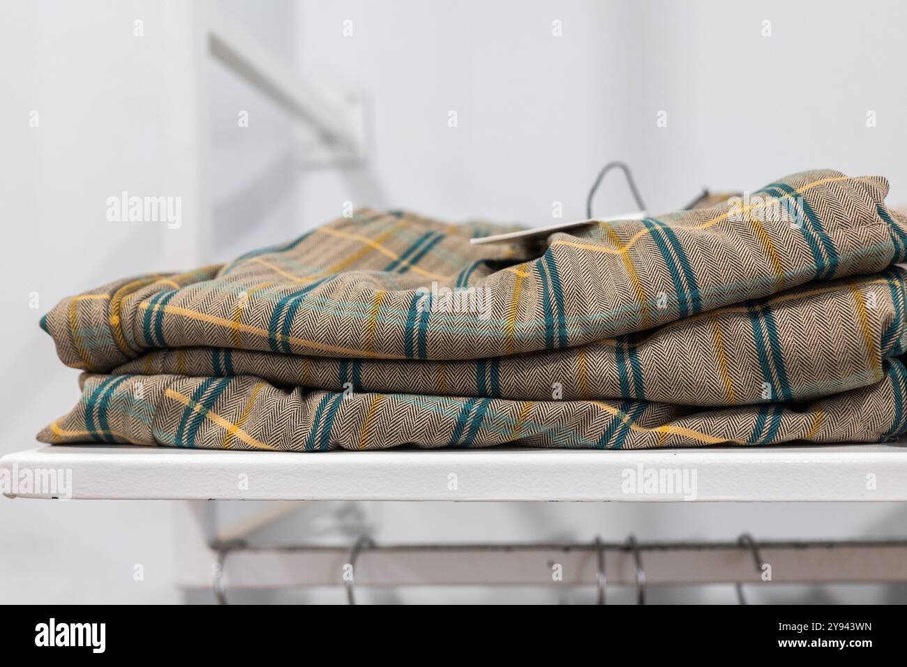 Une pile soigneusement arrangée de pantalons à carreaux à la mode dans les tons vert, jaune et marine, affiché sur une étagère blanche propre dans un magasin de vêtements, mettant en vedette c Banque D'Images