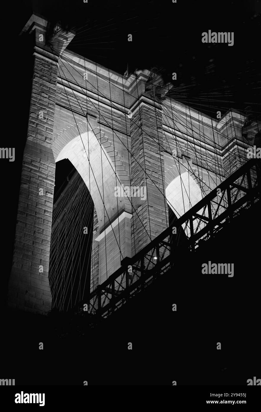 Vue nocturne d'une arche illuminée du pont de Brooklyn à New York mettant en valeur sa beauté architecturale et ses détails structurels. Le noir et blanc Banque D'Images
