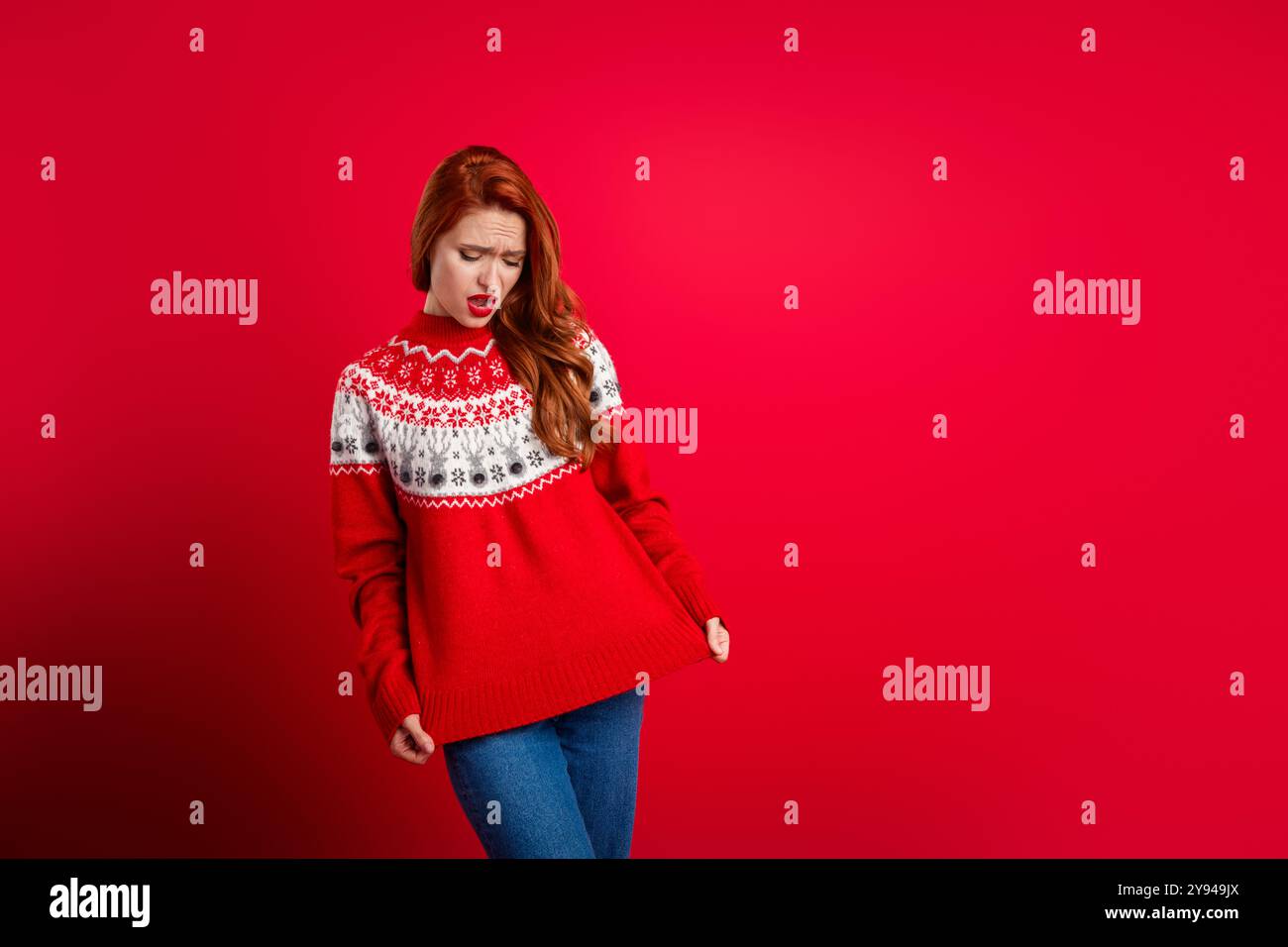 Photo de la jeune dame bouleversée démontrer son mauvais présent qu'elle n'aime pas le pull d'ornement pour les vacances du nouvel an isolé sur fond de couleur rouge Banque D'Images